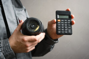 Calculation of the cost of installation of a video surveillance system concept. Video surveillance service worker holds a cctv security camera and calculator close up.
